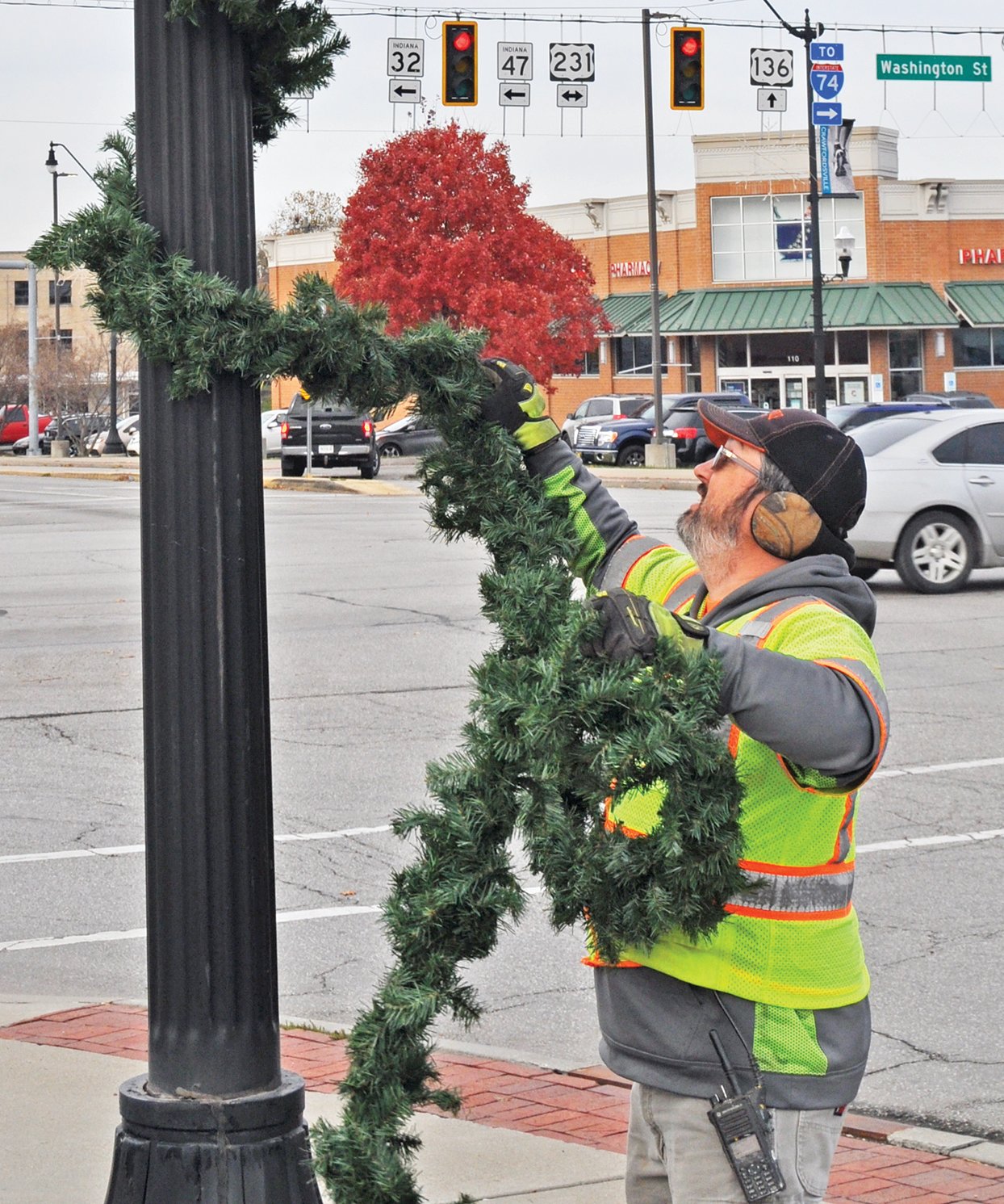 Chris Hartman of the Crawfordsville Street Department wraps garland around a light pole on East Market Street Tuesday. The street department was hanging holiday decorations in the downtown area.